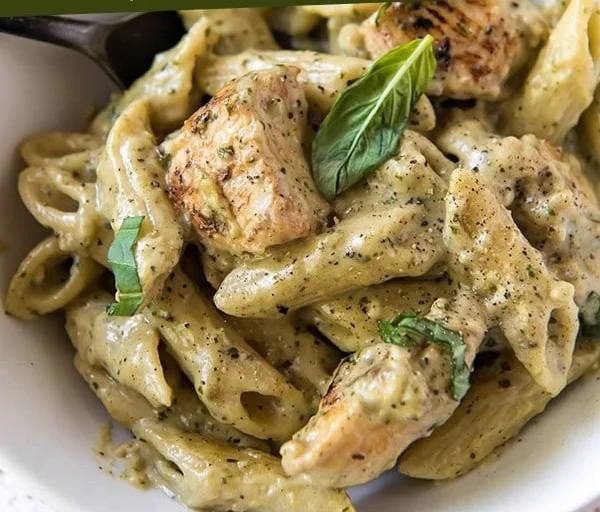 A delicious plate of cheesy pesto chicken pasta with fresh basil and cheese.