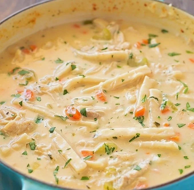 Bowl of creamy chicken noodle soup garnished with herbs and vegetables
