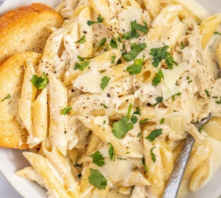 Creamy Crockpot Chicken Alfredo served with pasta and garnish.