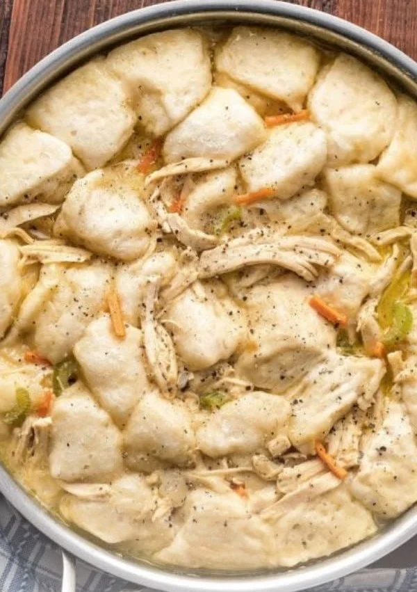 Bowl of easy chicken and dumplings with biscuits, garnished with parsley.