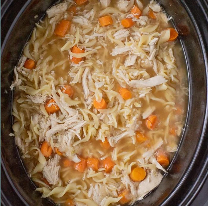 High protein chicken noodle soup in a bowl, garnished with herbs.