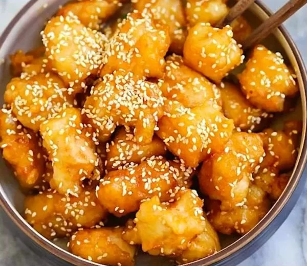 Plate of honey sesame chicken garnished with sesame seeds and green onions