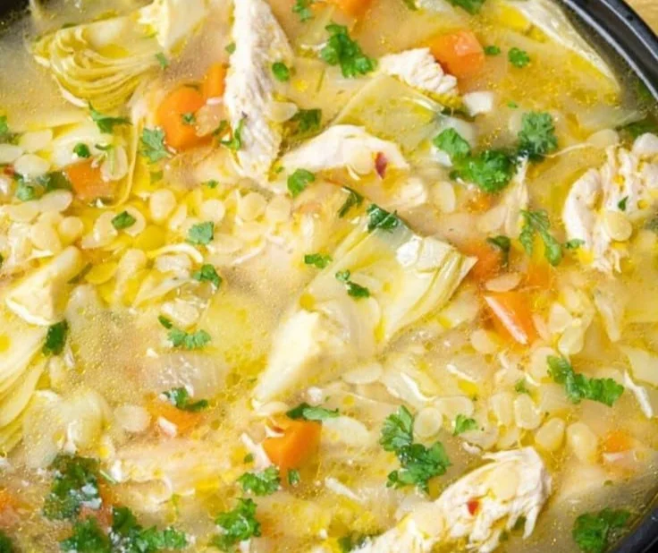 Bowl of Lemon Artichoke Chicken Soup garnished with herbs and lemon slices.