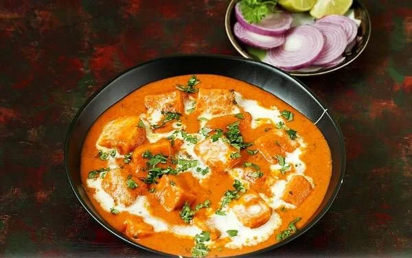 Delicious paneer butter masala served with naan and garnished with coriander.
