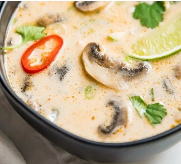 A bowl of authentic Tom Kha Soup with ingredients like coconut milk, herbs, and spices