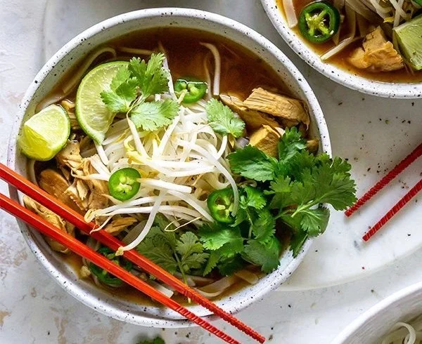 A bowl of Vietnamese Chicken Pho garnished with fresh herbs and lime.