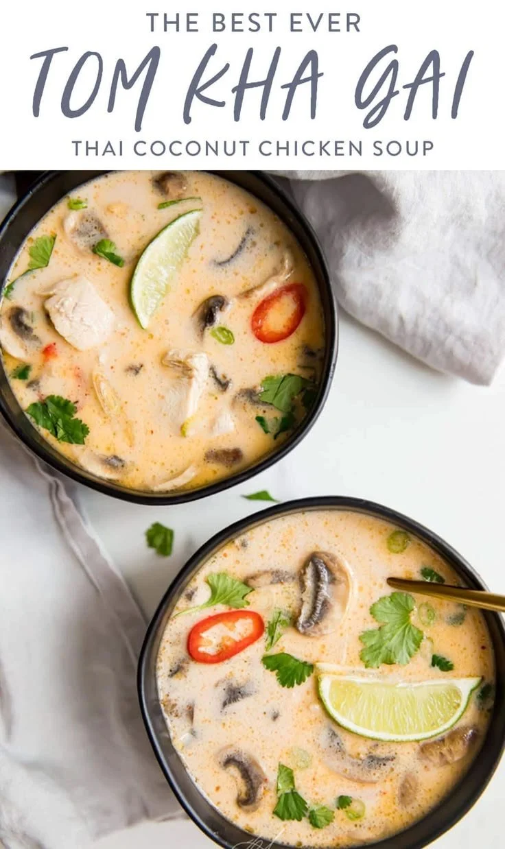 Bowl of Tom Kha Gai soup with chicken and herbs on a wooden table