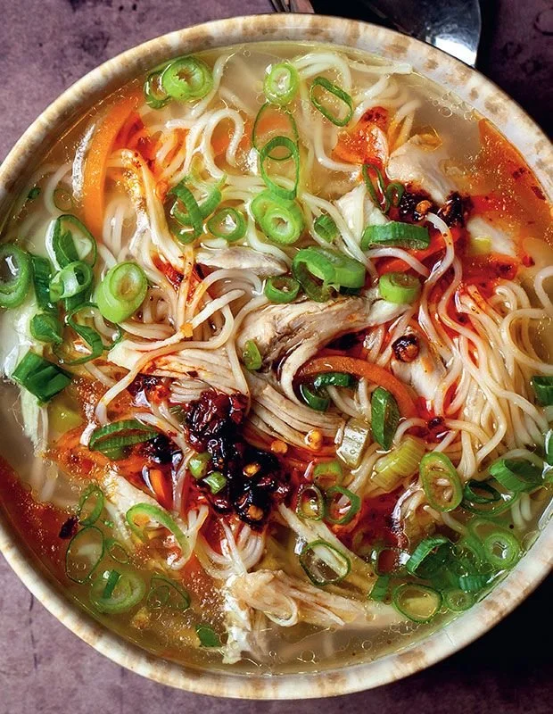A bowl of Ginger Garlic Chicken Noodle Soup with fresh herbs and spices.