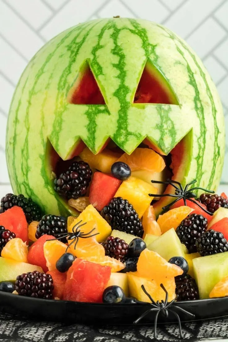 Colorful Halloween fruit salad with Halloween-themed decorations for a festive party.